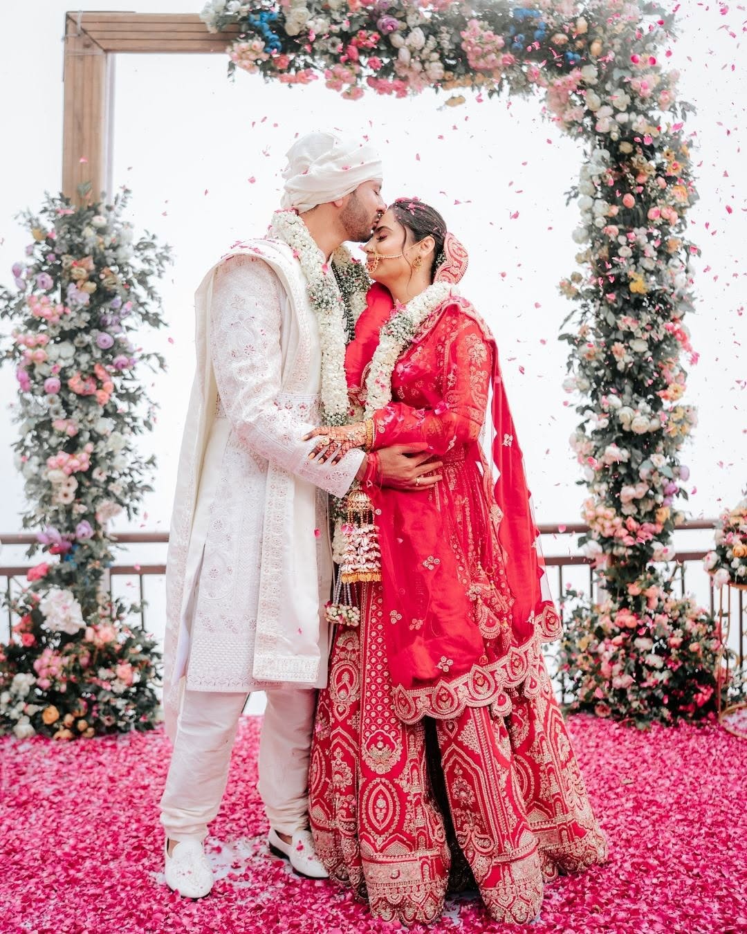 Couple sharing a kiss beneath a floral arch as petals fall
